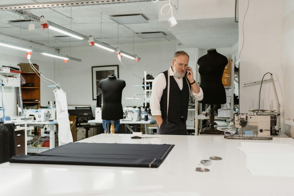 Tailor discussing work on phone in a modern fashion studio filled with sewing machines.
